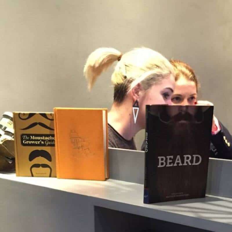 Two women with a mirror and books, one with a blonde ponytail, in a room.