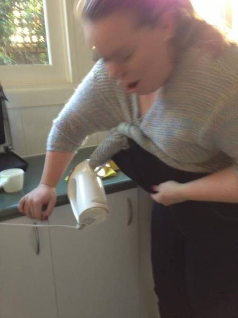 Woman with hair tied back holding a hairdryer near her face in a kitchen.