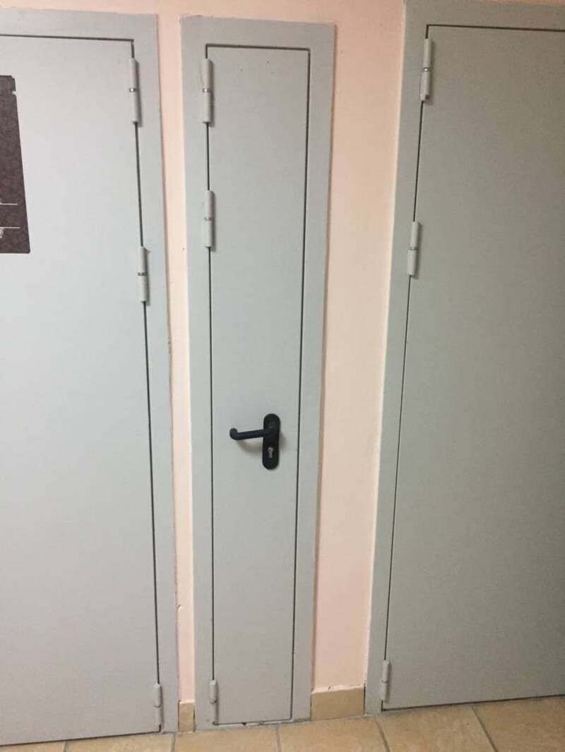 Small door between two larger doors, all painted gray, with a black handle.