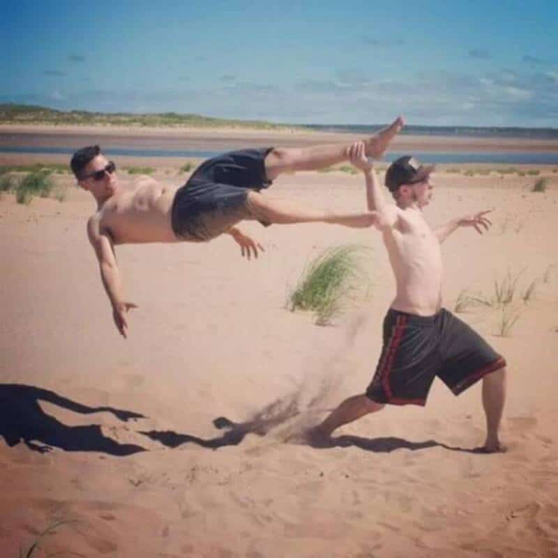 Two men on a beach, one holding the other's leg as he flies through the air.