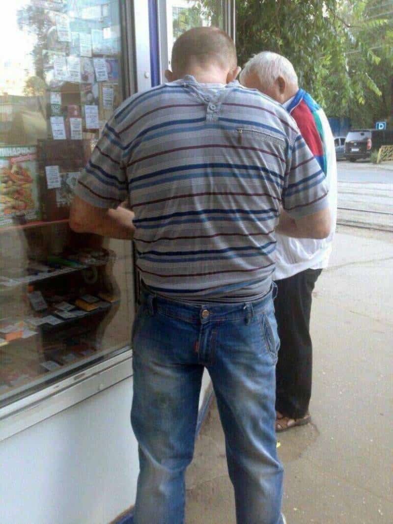 Two men standing outside a store, one with his back to the camera, the other facing away.