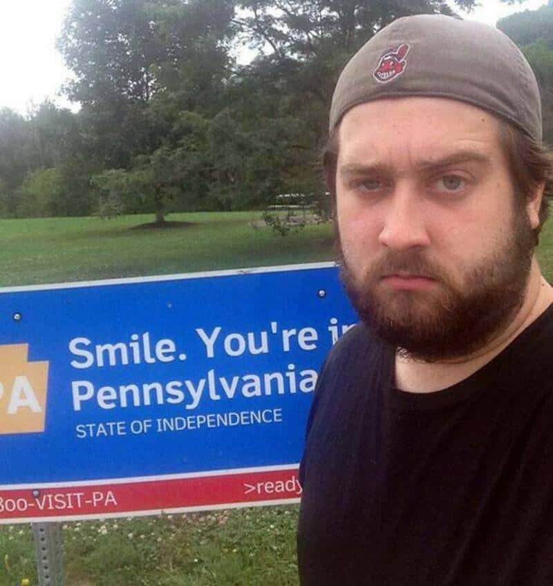Man with a beard and gray cap standing near a Pennsylvania sign.