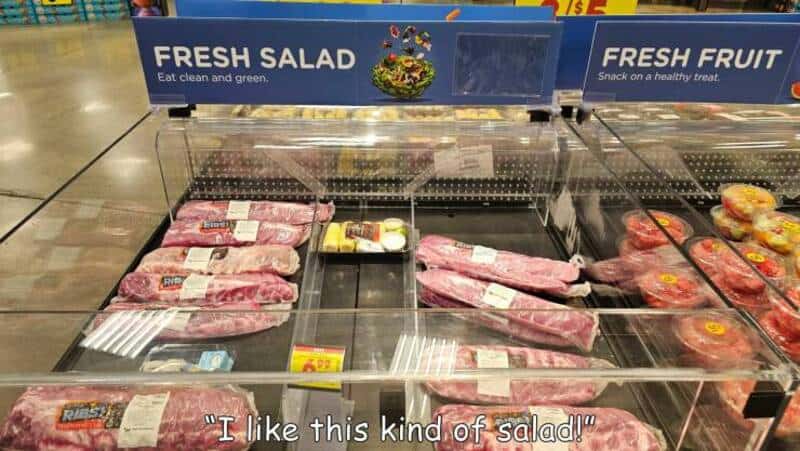 Meat cuts in a supermarket with a sign for fresh salad and fruit.