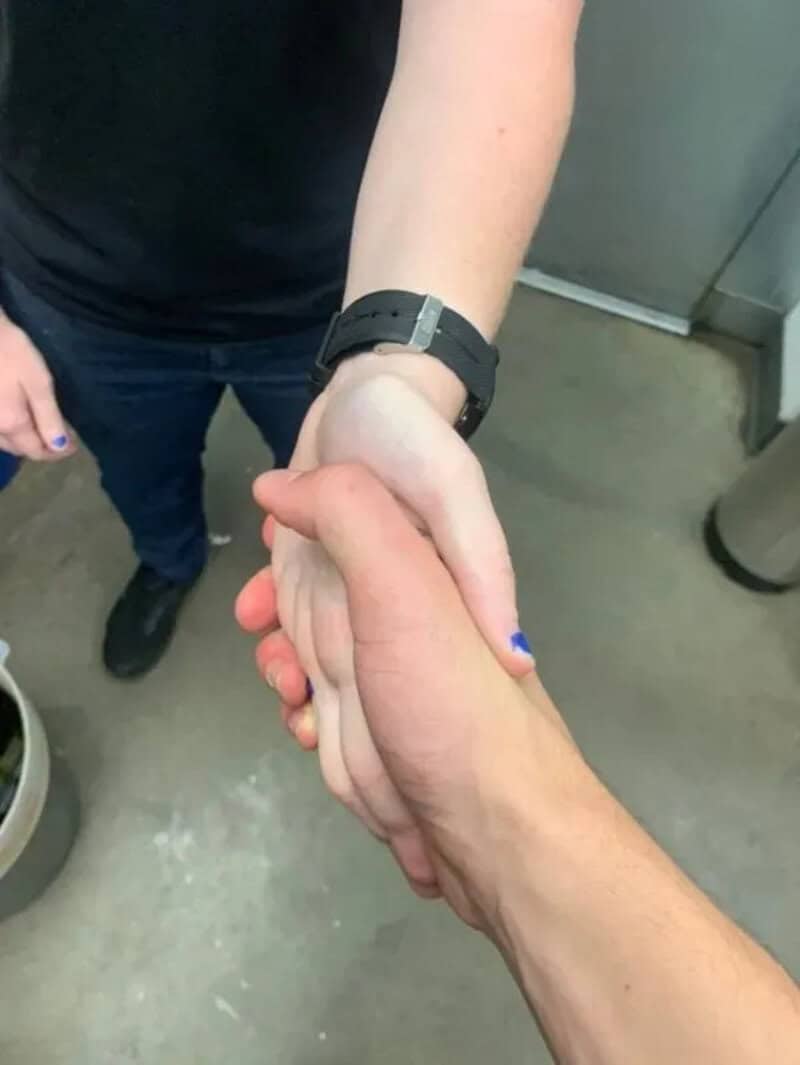 Two people shake hands, one with a black watch, in an indoor setting.