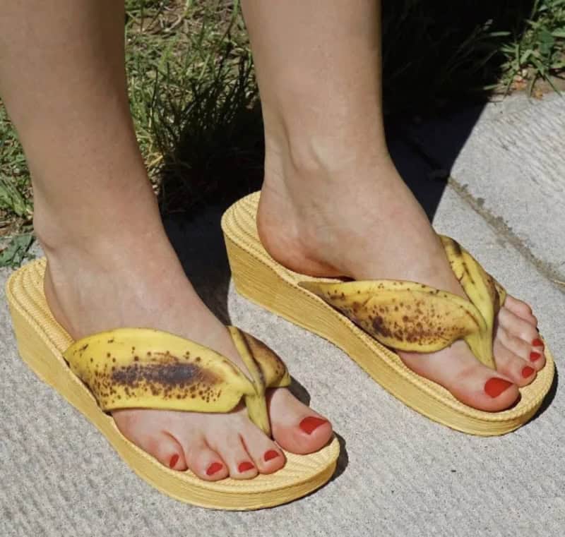 Person wearing banana-shaped sandals with red toenail polish on a sidewalk.