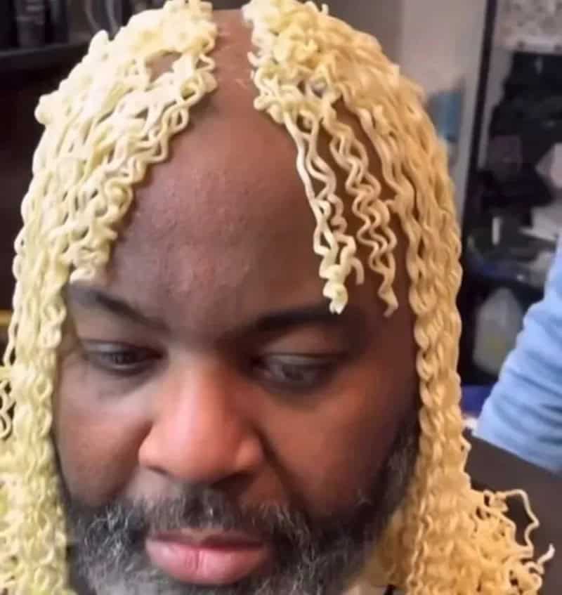 Person with curly blonde hair made of instant ramen noodles, looking down.