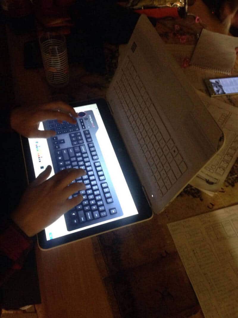 Child using a tablet with a keyboard attachment, surrounded by papers and a phone.