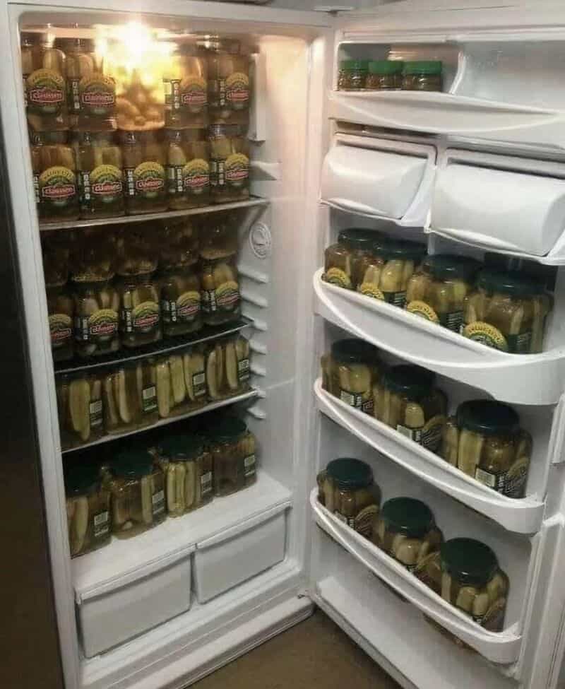 Open fridge filled with jars of mustard and pickles, some on shelves and others in door compartments.