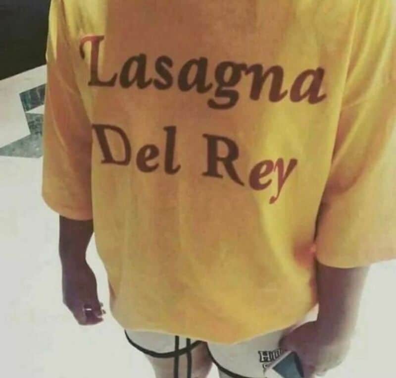 T-shirt with 'Lasagna Del Rey' text, person holding a phone, background not visible.