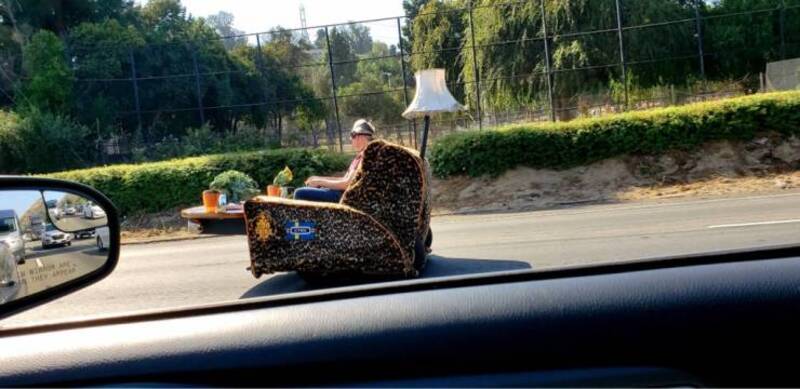 Person sitting in a chair on the back of a moving vehicle on the highway.