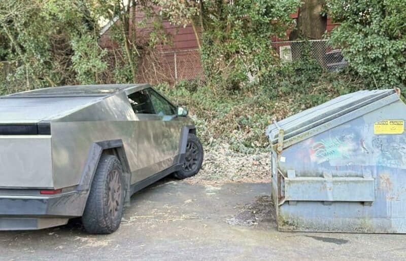 A futuristic-looking gray car parked next to a large blue dumpster.