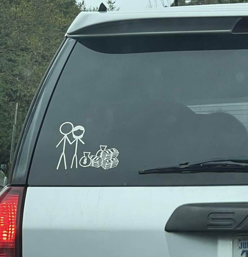Stick figure drawing of two people with money and a piggy bank on car window.
