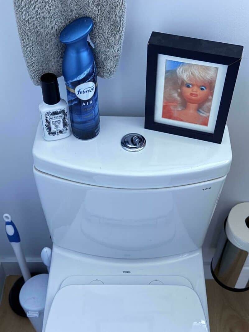Toilet with framed doll photo, Febreze air freshener, and hand sanitizer on top.