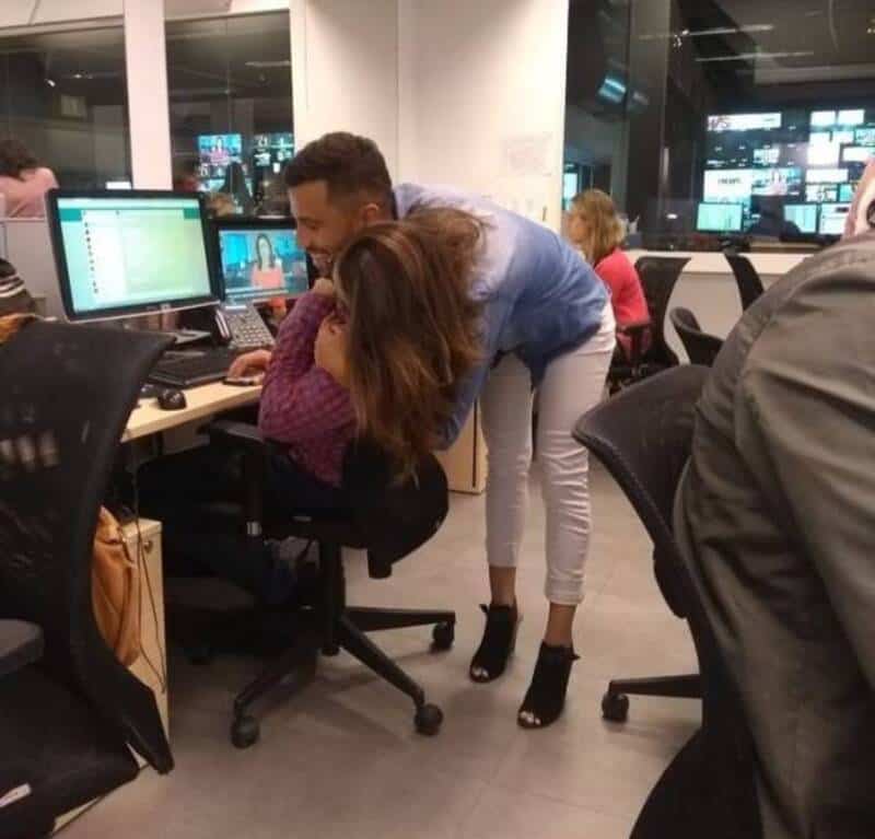 Woman leaning over to talk to a seated woman at a computer in an office.