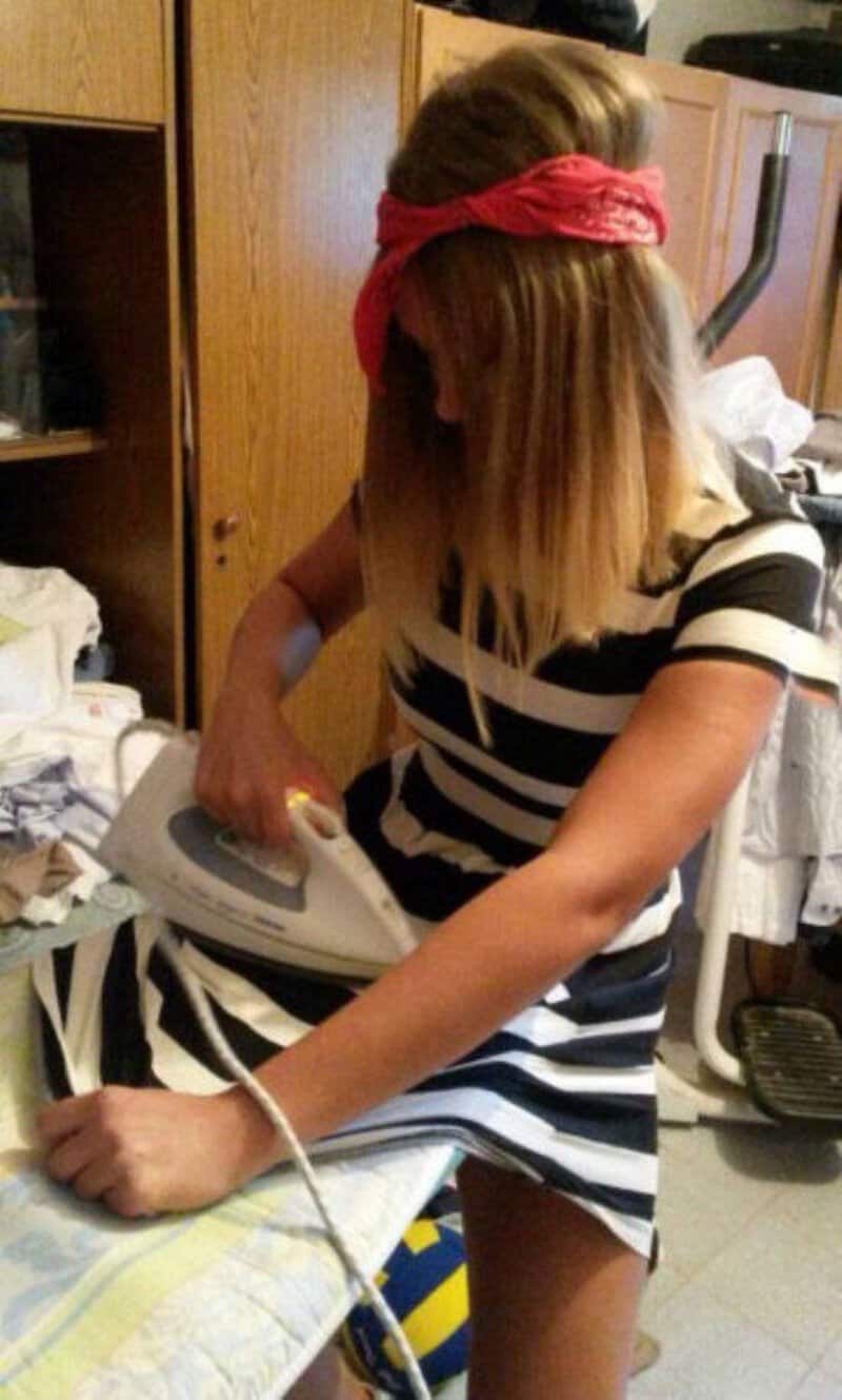 Girl with a red headband ironing clothes in a laundry room.