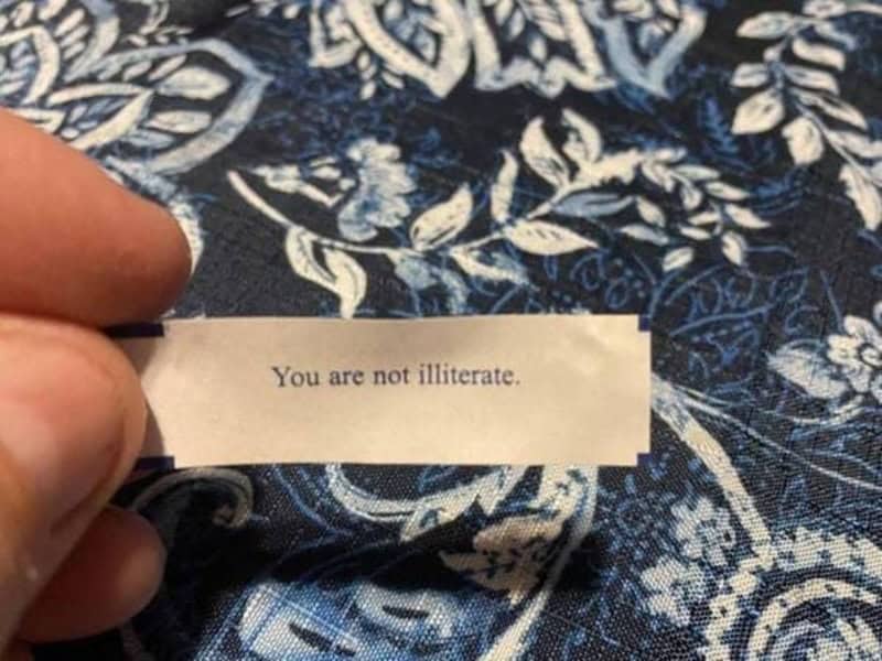 A hand holding a note that says 'You are not illiterate.' on a blue patterned fabric.