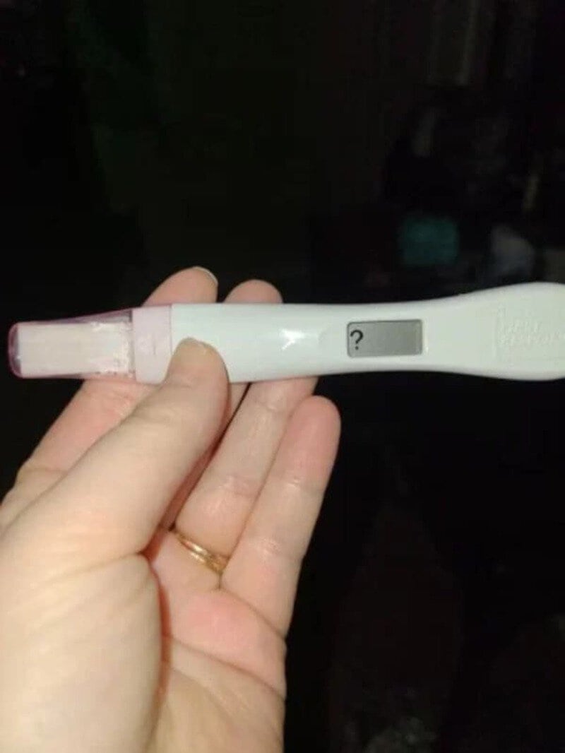 Hand holding a pregnancy test with a question mark on the display.