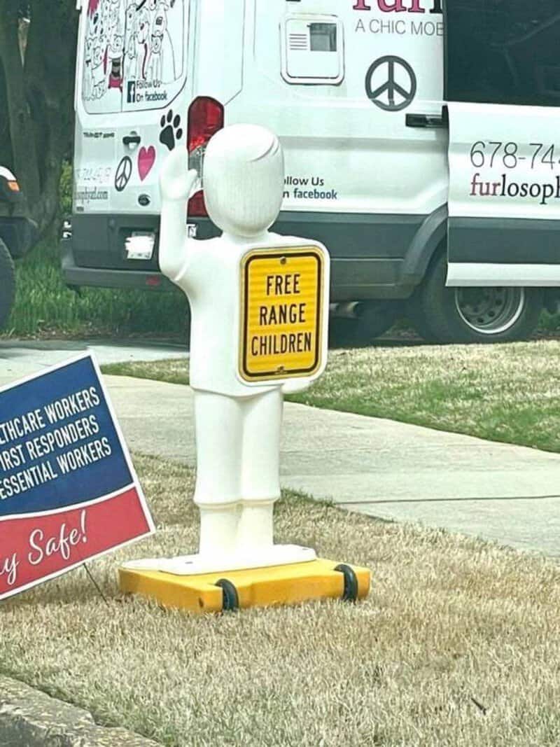A white statue of a child holding a yellow sign that says 'FREE RANGE CHILDREN'.