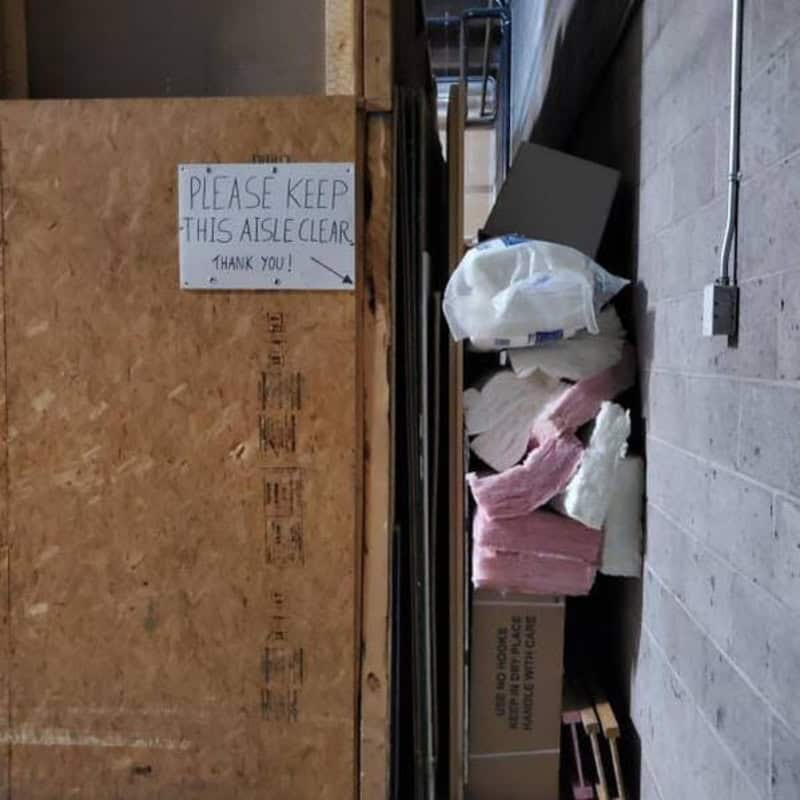 Cluttered storage aisle with a sign asking to keep it clear.