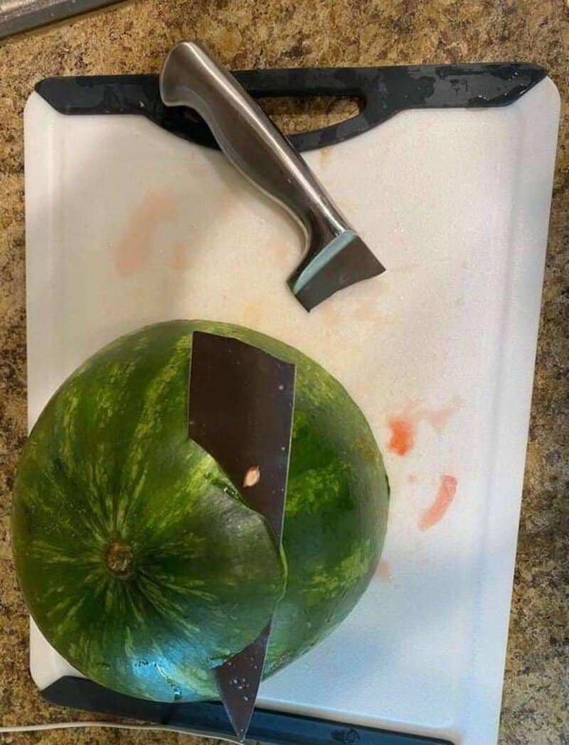 Watermelon with a knife and hammer on a cutting board.