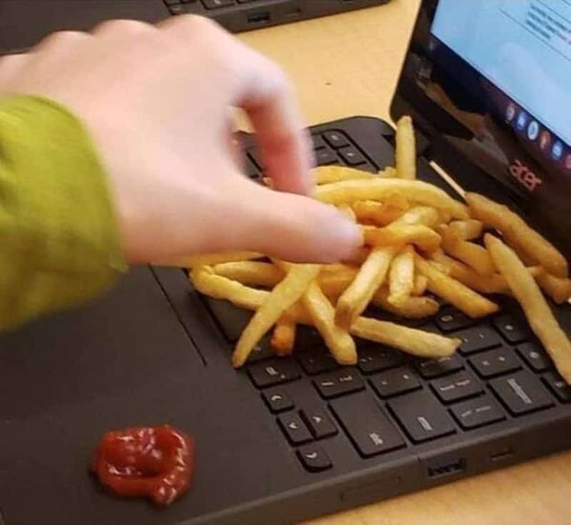 French fries on a laptop keyboard with a hand reaching for them.