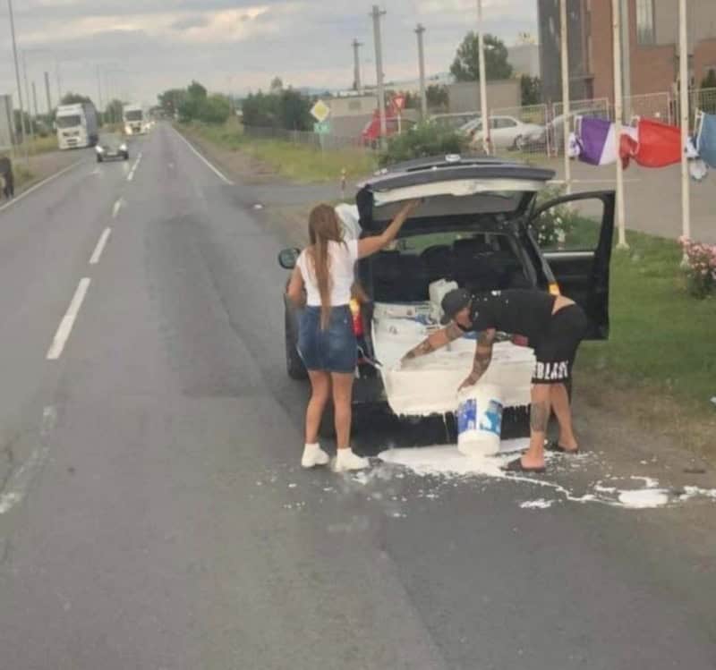 People cleaning a car with spilled paint on the road.