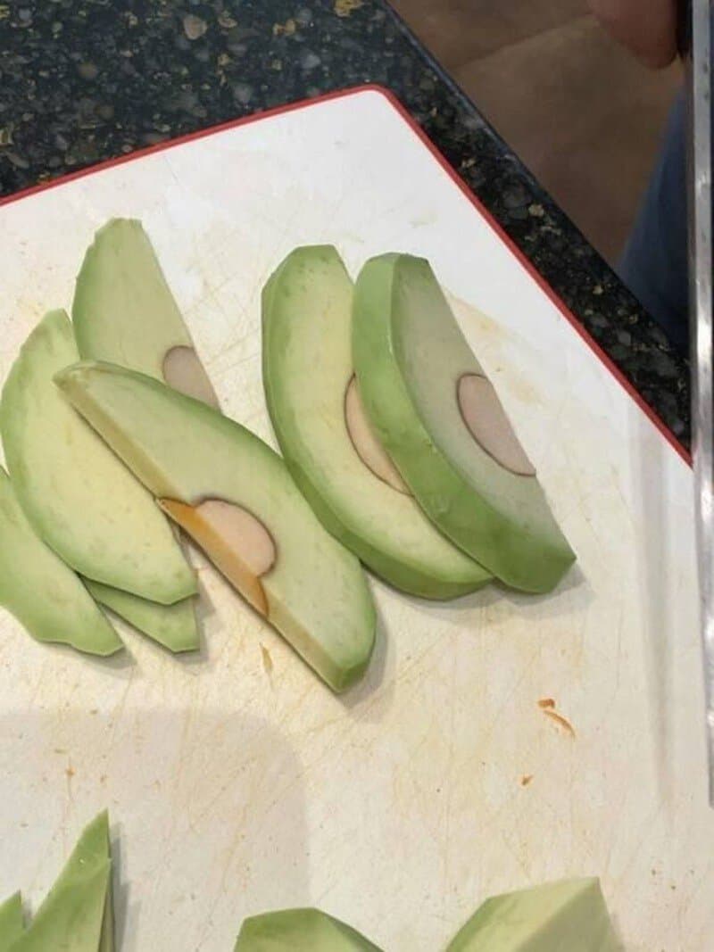 Sliced avocado with a humorous face shape on a cutting board.