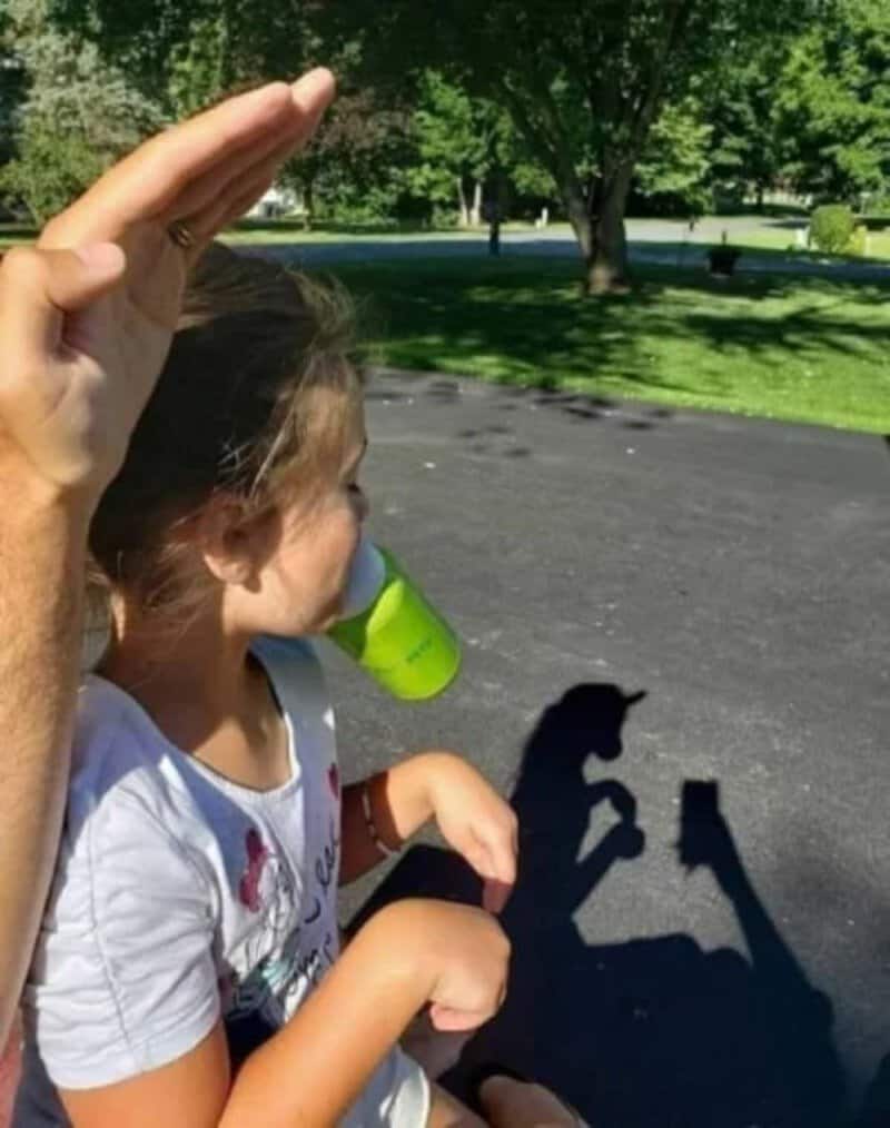 Child with a green cup and shadow of a hand making a peace sign.