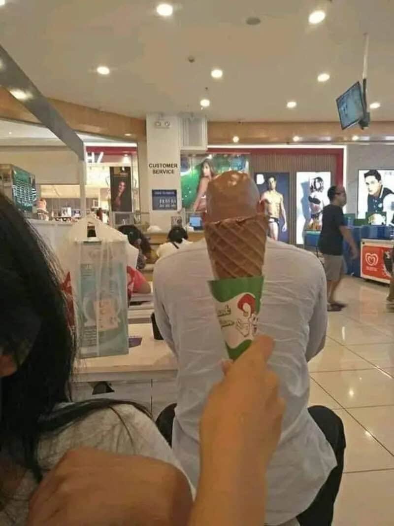 Ice cream cone in front of a man at a shopping mall.