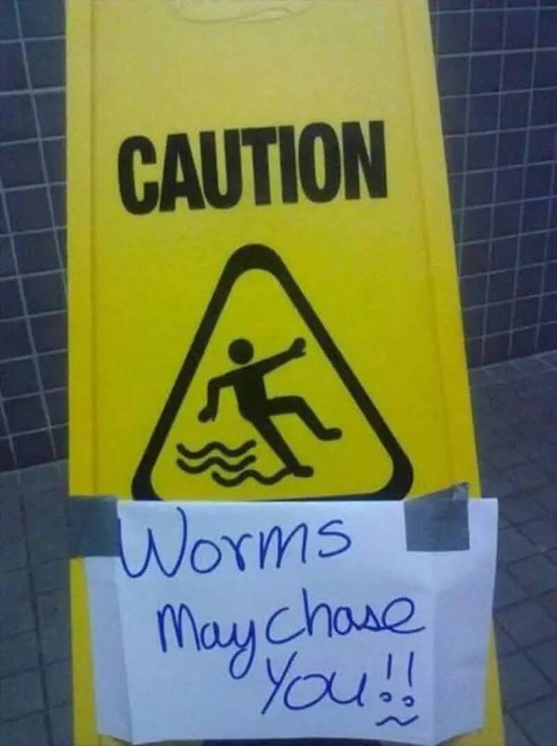 Caution sign with a person falling into water, handwritten note says 'Worms May Chase You!!'.