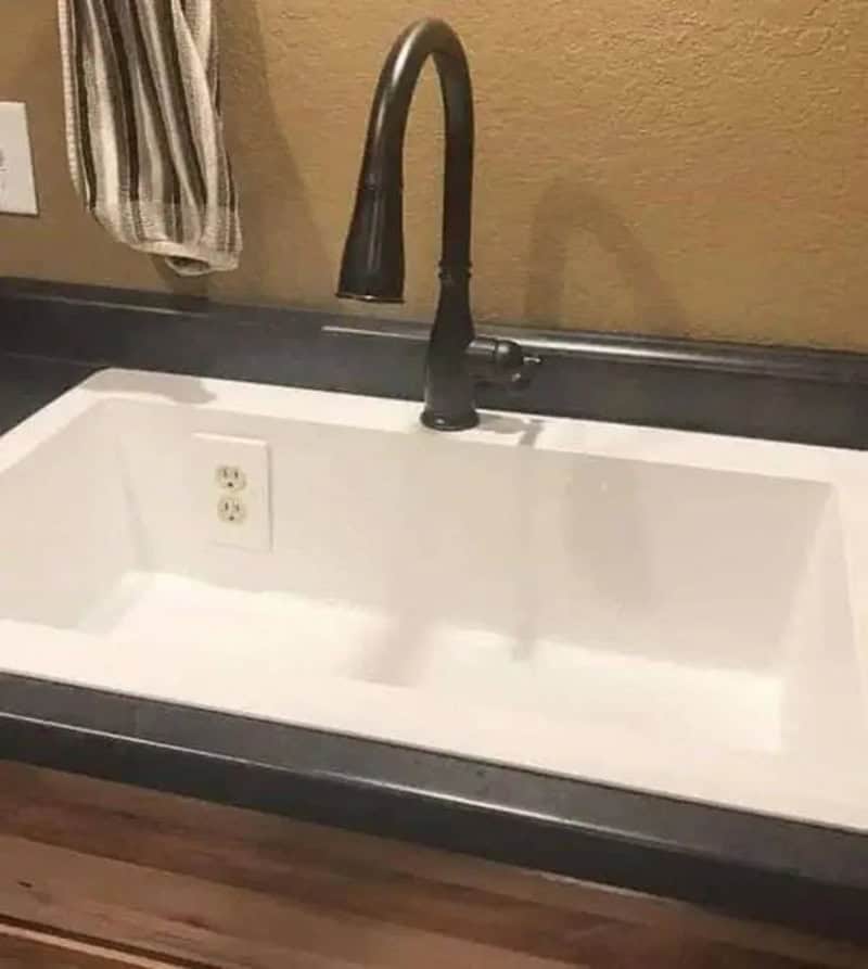 Empty kitchen sink with a black faucet and a striped towel hanging nearby.