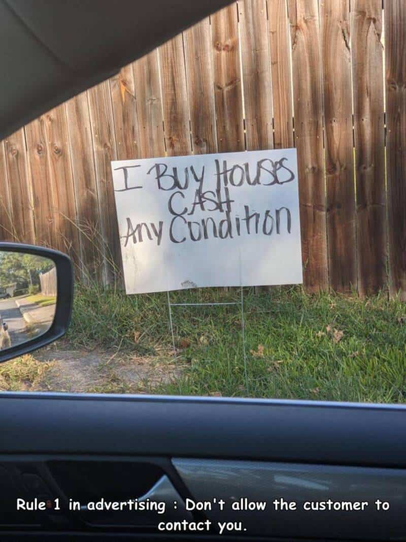 Sign says 'I buy house as is, any condition' in front of a wooden fence.