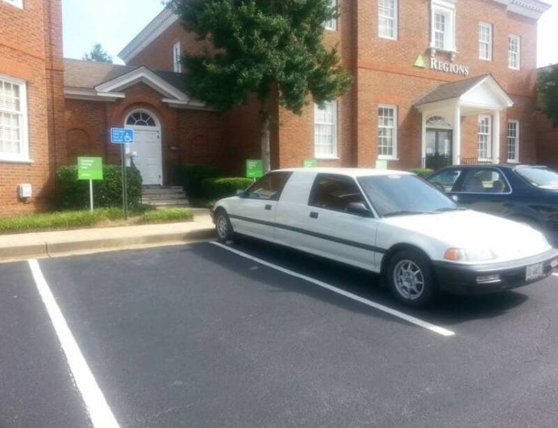 White car parked in a parking lot in front of a brick building.