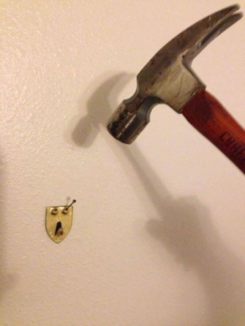 Hammer about to hit a small keyhole on a wall.