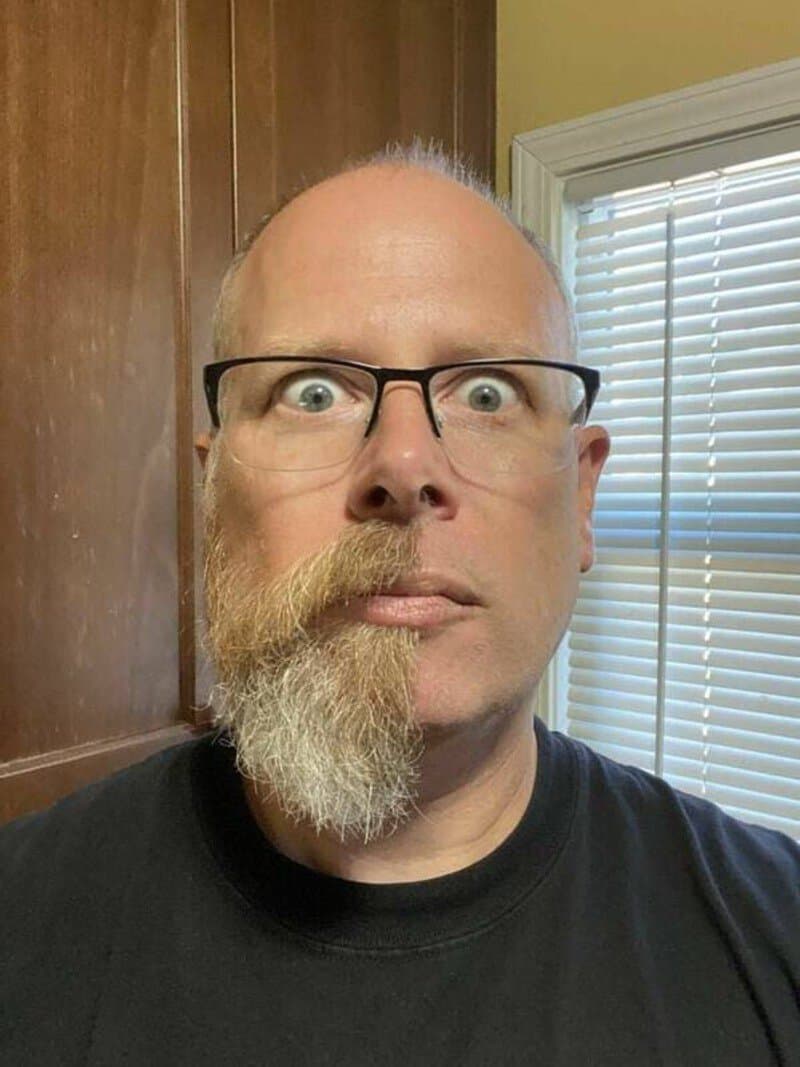 Man with half beard and glasses making a funny face in a kitchen.