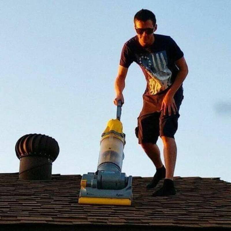 Man cleaning roof with vacuum cleaner, wearing sunglasses and casual clothes.