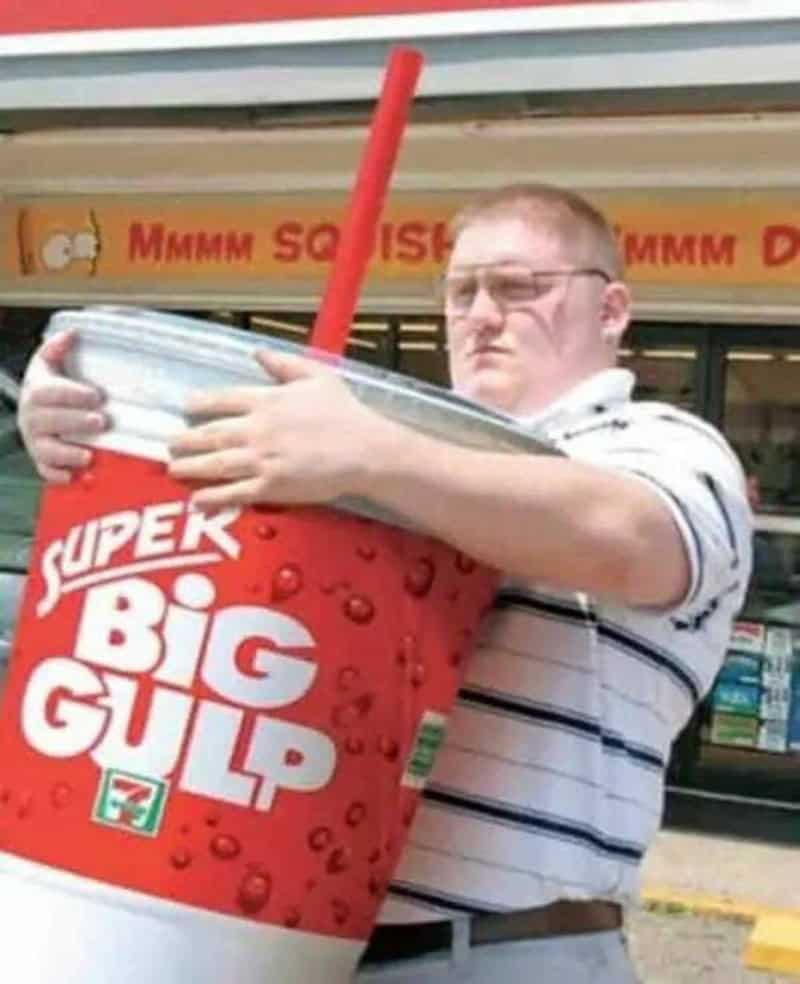 Man holding a giant cup of Big Gulp soda outside a store.