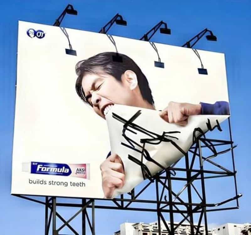Billboard ad showing a woman biting a giant toothbrush with black braces.