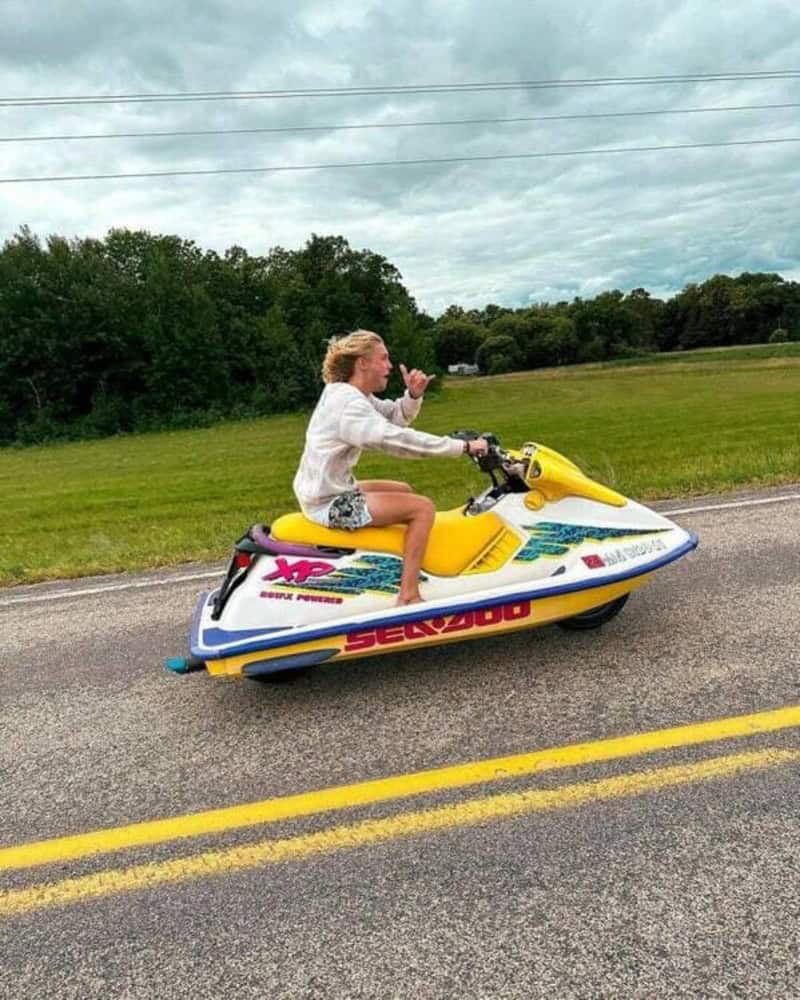 Girl riding a yellow and white jet ski on the road, waving.