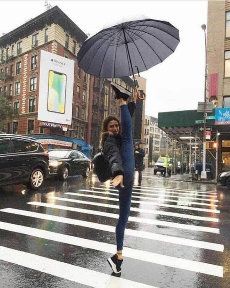 Person holding an umbrella while doing a handstand on a crosswalk in the rain.