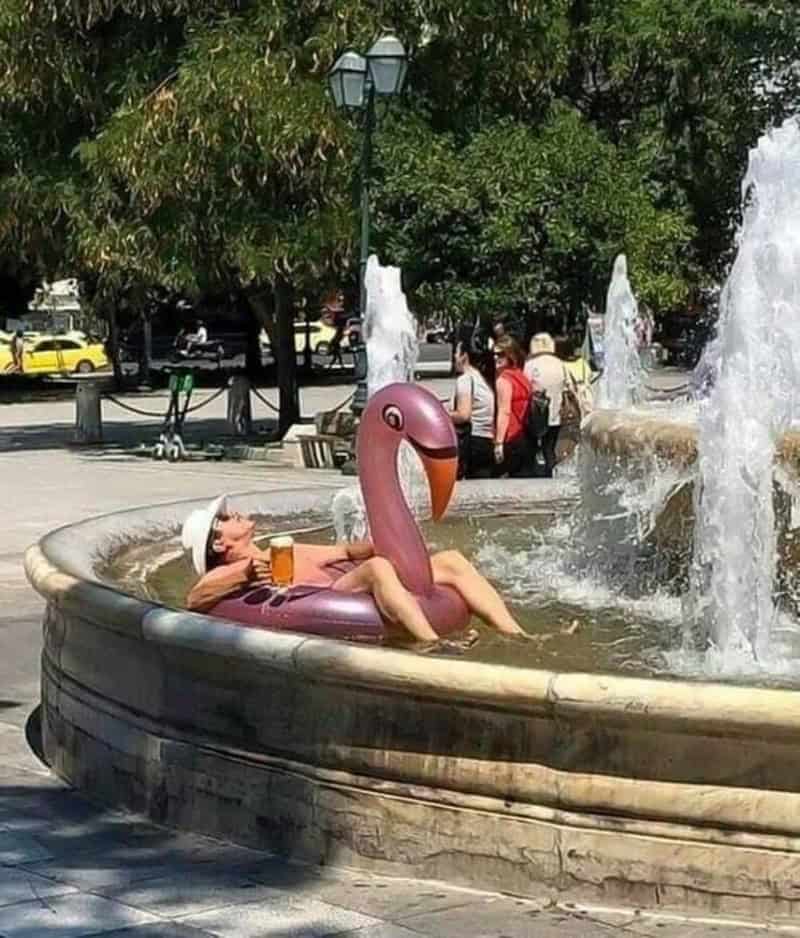 Person relaxing on a flamingo float in a fountain with water splashing.