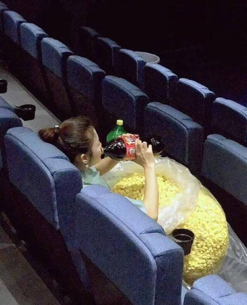Girl drinking soda in a movie theater with a large bucket of popcorn.