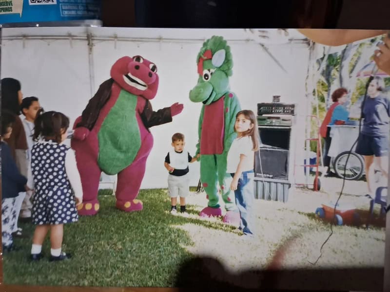 Children with costumed characters of a pink bear and a green dragon at a fair.