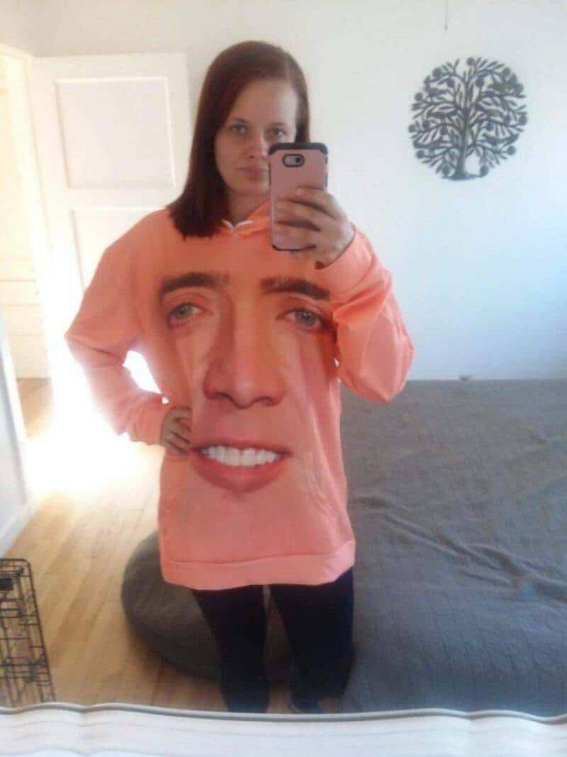 Woman wearing a sweatshirt with a large face print, taking a mirror selfie.