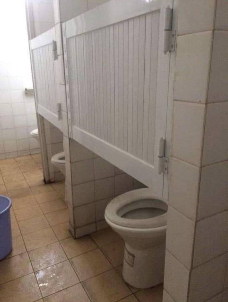 Toilet in a bathroom with a privacy partition and a blue bucket nearby.