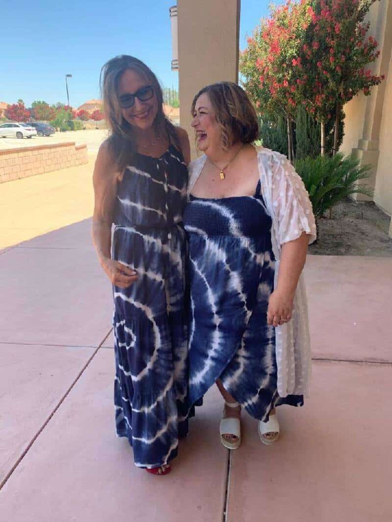 Two women in tie-dye dresses laughing outside on a sunny day.