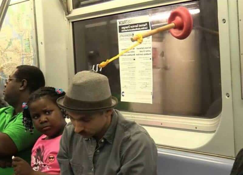 Man with a plunger hitting a window on a train, with children nearby.