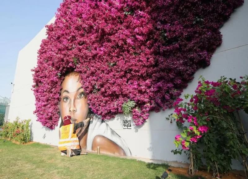 Mural of a woman with pink flowers covering her hair on a white wall.