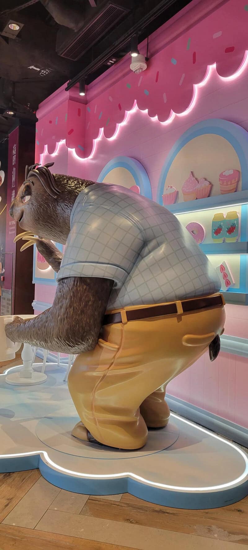 Humanoid bear in a bakery store wearing a checkered shirt and yellow pants.
