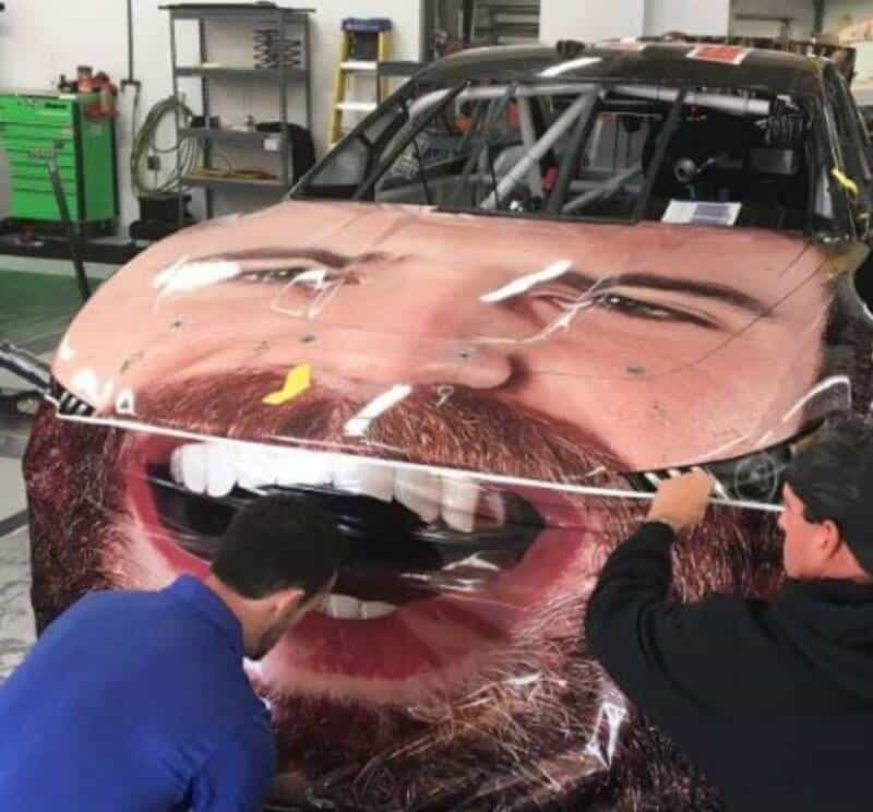 Car with a large smiling face printed on the hood, two men working on it.